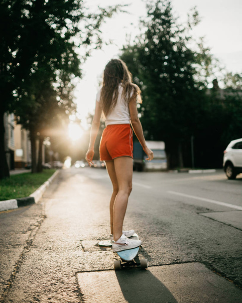 Beautiful skater woman riding on her longboard in the sunset cit - Photo, Image