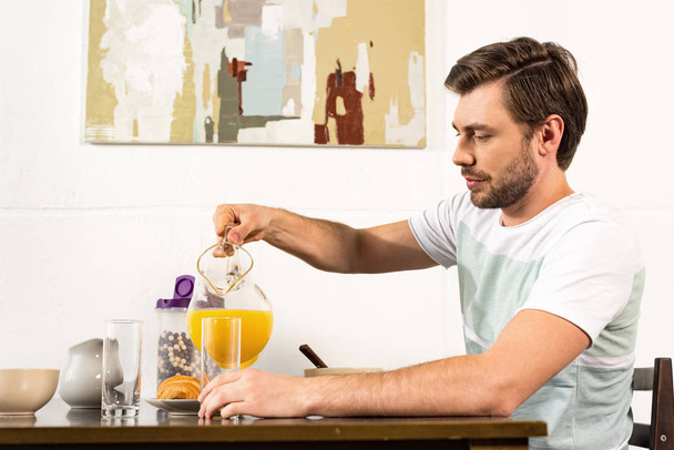 man pouring orange juice in glass during breakfast in kitchen - Zdjęcie, obraz