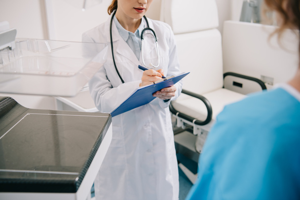 vista recortada del médico escribiendo en el portapapeles mientras está de pie cerca del paciente
  - Foto, Imagen