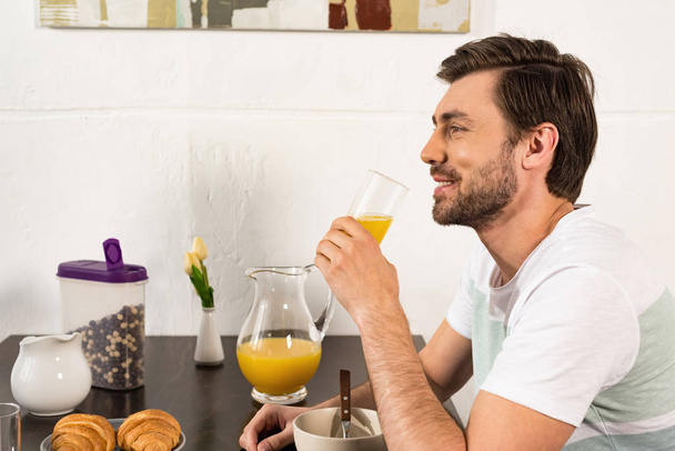 smiling bearded man holding glass of orange juice during breakfast - Zdjęcie, obraz