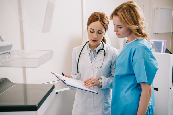 attractive young doctor and patient looking at diagnosis on clipboard - Photo, Image