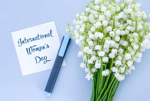 A felirat nemzetközi nőnap papíron, a marker és a csokor gyöngyvirág a völgy kék háttér - Fotó, kép