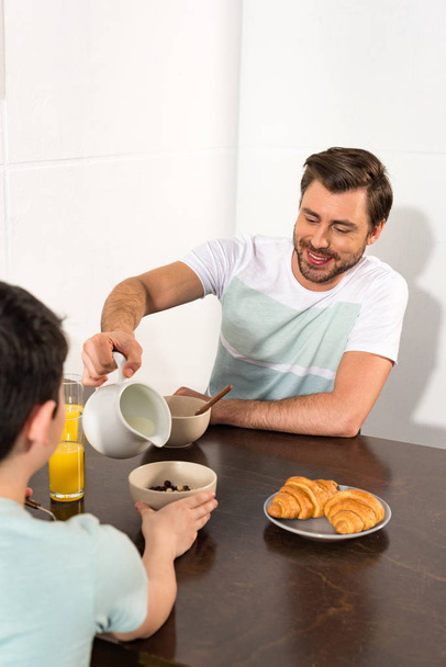 dad pouring milk in bowl during breakfast with son - Фото, изображение