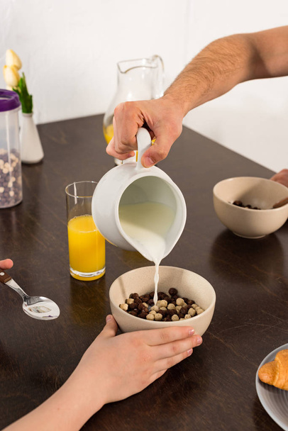 обрезанный вид, как папа наливает молоко в миску во время завтрака с сыном
 - Фото, изображение