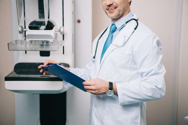 partial view of doctor holding clipboard while standing at x-ray machine - Fotografie, Obrázek