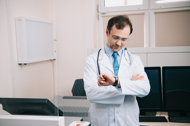 όμορφος γιατρός σε λευκό παλτό και γυαλιά Έλεγχος χρόνου στο ρολόι  - Φωτογραφία, εικόνα