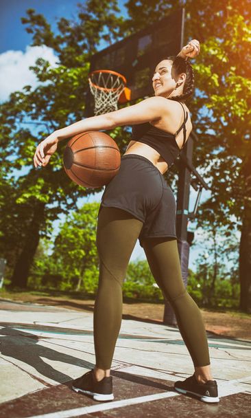 Красива сексуальна фітнес-дівчина в чорному спортивному одязі з ідеальним тілом з кошиком на баскетбольному майданчику. Спорт, фітнес, концепція способу життя
 - Фото, зображення