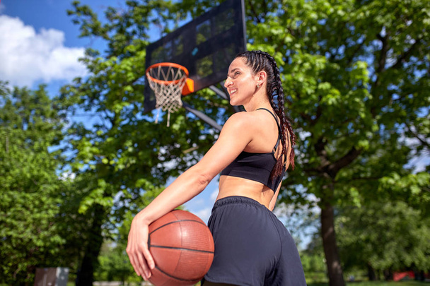 Beautiful sexy fitness girl in black sport wear with perfect body with basket ball at basketball court. Sport, fitness, lifestyle concept - Fotografie, Obrázek