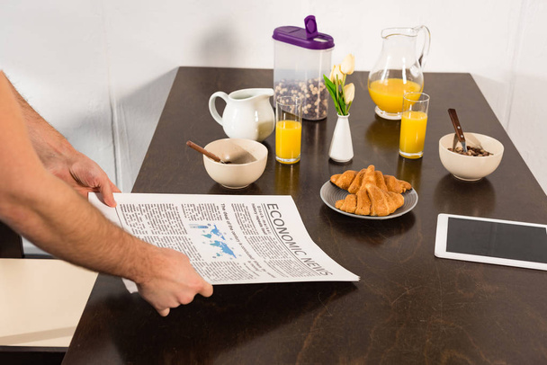 cropped view of man holding newspaper during breakfast in kitchen - Foto, Imagem