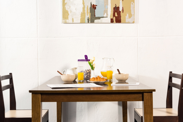 chairs and table with orange juice, croissants and breakfast cereal in kitchen - Photo, Image
