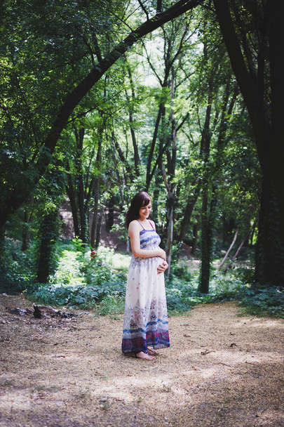 カラフルな夏の森のライトドレスで妊娠中の女性の美しい肖像画。妊娠の概念と年の時間。フィルム加工. - 写真・画像