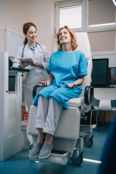 valikoiva painopiste onnellinen nainen istuu nojatuolissa lähellä hymyilevä lääkäri tilalla digitaalinen tabletti
 - Valokuva, kuva