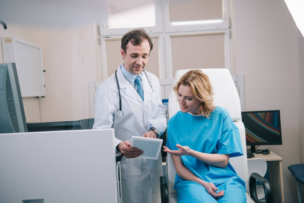 selective focus of handsome doctor showing digital tablet to smiling woman - Photo, Image
