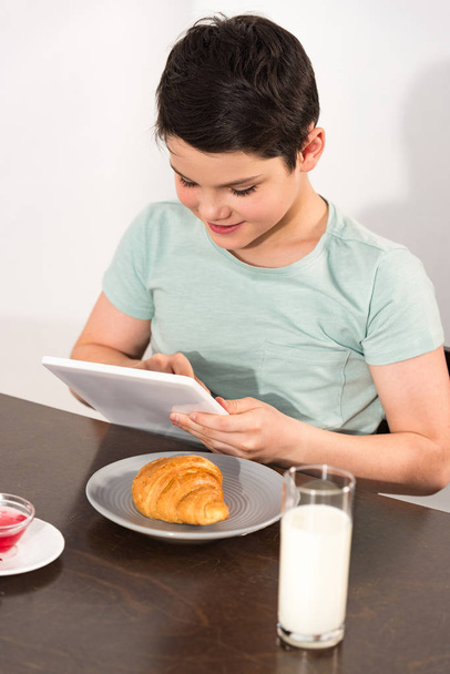 smiling boy using digital tablet during breakfast in kitchen - Fotó, kép