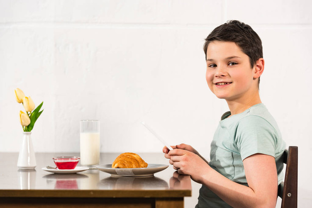 ragazzo sorridente utilizzando tablet digitale durante la colazione in cucina
 - Foto, immagini