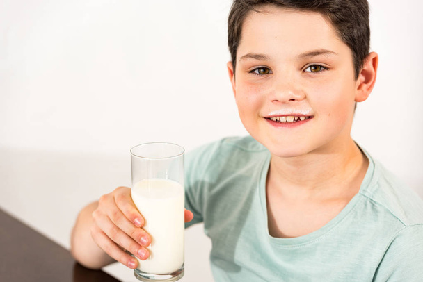 usměvavý chlapec držící sklenici mléka a pohled na kameru - Fotografie, Obrázek