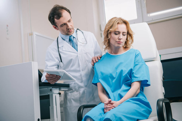 attentive doctor touching shoulder of upset woman while holding digital tablet - Photo, image