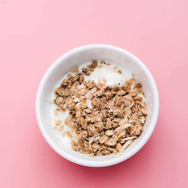 Whole grains on yogurt in white bowl, pink background. - Foto, imagen