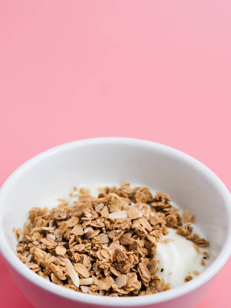 Whole grains on yogurt in white bowl, pink background. - Фото, изображение