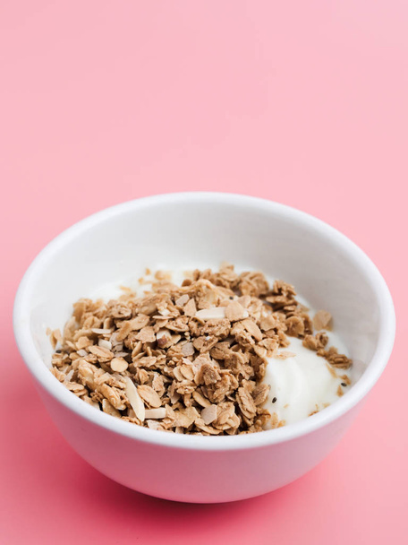Whole grains on yogurt in white bowl, pink background. - Фото, изображение