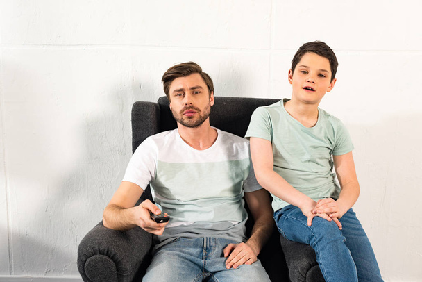 son and father with remote controller watching tv in living room - Foto, afbeelding