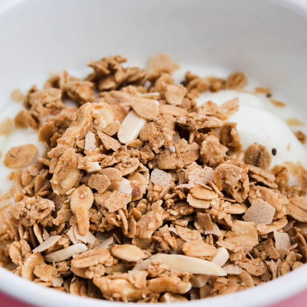 Whole grains on yogurt in white bowl, pink background. - Foto, imagen