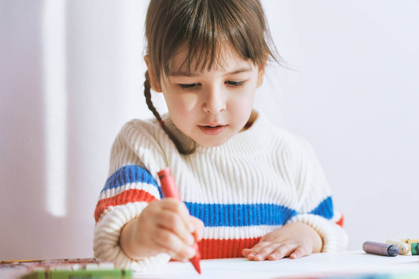 Creative little girl painting with colorful pencils, sitting at white desk at home. Joyful child drawing with pencils. People, childhood and education concept - Photo, Image