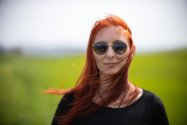 緑の草原に立つサングラスをかけた生姜の髪の女性 - 写真・画像