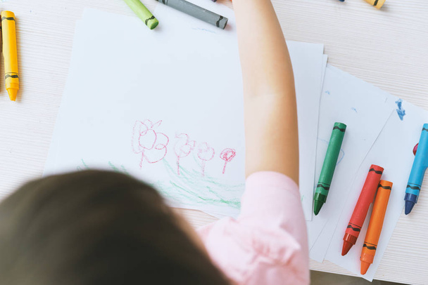 Top view image of hands of little girl drawing with colorful pencils, dressed in pink t-shirt. Pretty preschooler child painting and learning at kindergarten. People, childhood, education - Foto, Imagen
