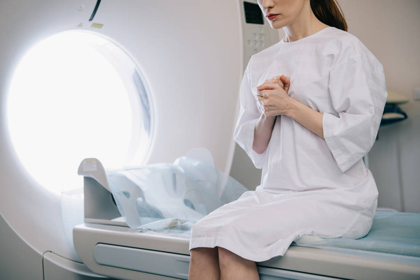 vista recortada de la mujer que muestra gesto de oración mientras está sentado en la cama del escáner de tomografía computarizada
 - Foto, Imagen