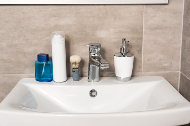 lotion, shaving foam, liquid soap and brush on sink in bathroom - Фото, зображення