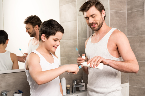 son and dad applying toothpaste in morning in bathroom - Фото, зображення