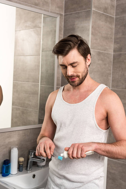 усміхнений чоловік наносить зубну пасту на тобруш вранці у ванній
 - Фото, зображення