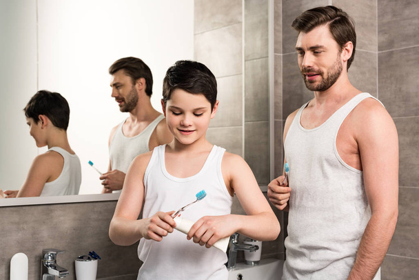 smiling son and dad with toothbrushes and toothpaste in bathroom - Foto, afbeelding