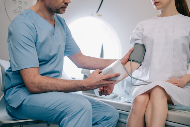 vue partielle du médecin mesurant la pression artérielle des patients avec un tonomètre lorsqu'ils sont assis au scanner ct
 - Photo, image