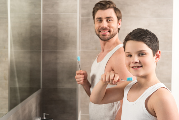 バスルームで朝に歯を磨く笑顔の息子とお父さん - 写真・画像