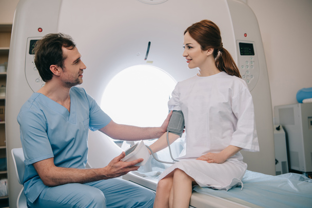 przystojny lekarz pomiaru ciśnienia krwi pacjentów z tonometru siedząc przy MRI skanera - Zdjęcie, obraz