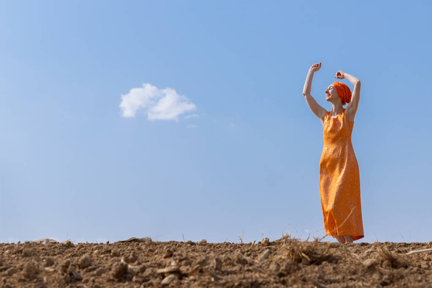 Ethnic Woman in Turban Dances on Clean Soil on Sky and Clouds Background - Valokuva, kuva