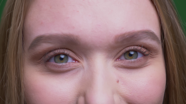 Ritratto dell'occhio di bella studentessa zenzero sorride gioiosamente in macchina fotografica su sfondo cromatico verde
. - Filmati, video