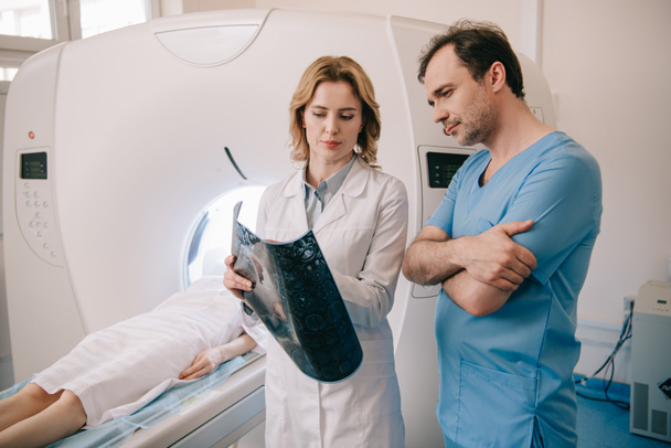 вдумчивые врачи смотрят на рентгеновскую диагностику во время диагностики пациентов на КТ-сканере
 - Фото, изображение