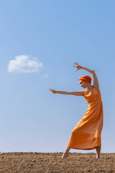 Ethnic Woman in Turban Dances on Clean Soil on Sky and Clouds Background - Zdjęcie, obraz