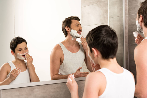 father and preteen son applying shaving foam in bathroom - Photo, image