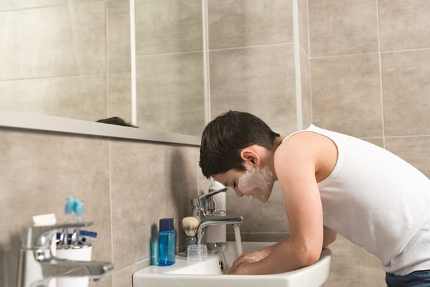 Preteen jongen wassen gezicht in de ochtend in de badkamer - Foto, afbeelding