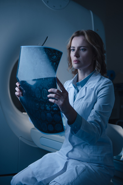 médecin sérieux regardant le diagnostic par rayons X tout en étant assis près ct scanner
  - Photo, image