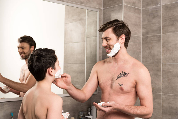 lachende Söhne und Väter, die im Badezimmer Rasierschaum auftragen - Foto, Bild