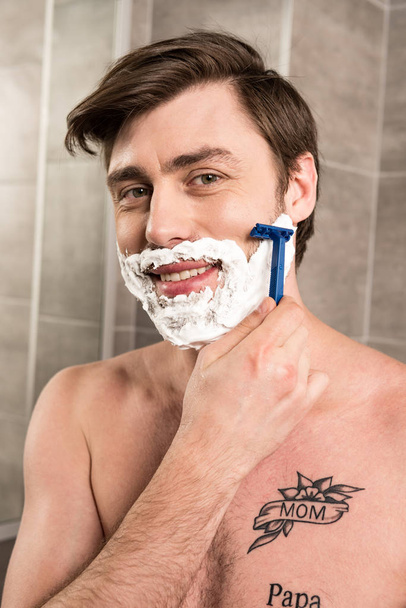 uśmiechnięty człowiek golenie brody z brzytwa w łazience - Zdjęcie, obraz