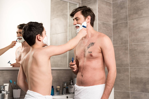preteen boy shaving father with razor in morning in bathroom - 写真・画像