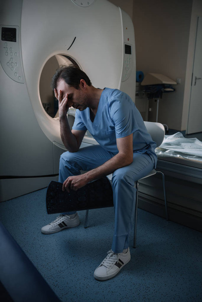 hastanede ct tarayıcı yakınında otururken x-ray tanısı tutan yorgun radyolog - Fotoğraf, Görsel