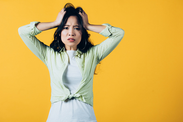 schöne gestresste asiatische Frau hält den Kopf isoliert auf gelb - Foto, Bild