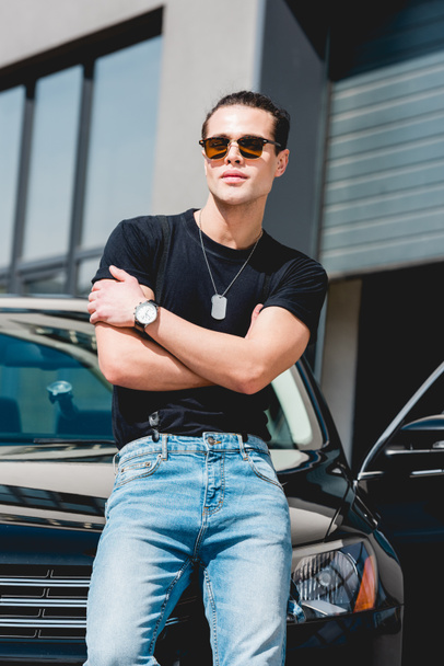 handsome stylish man in sunglasses posing near car with crossed arms - Fotoğraf, Görsel